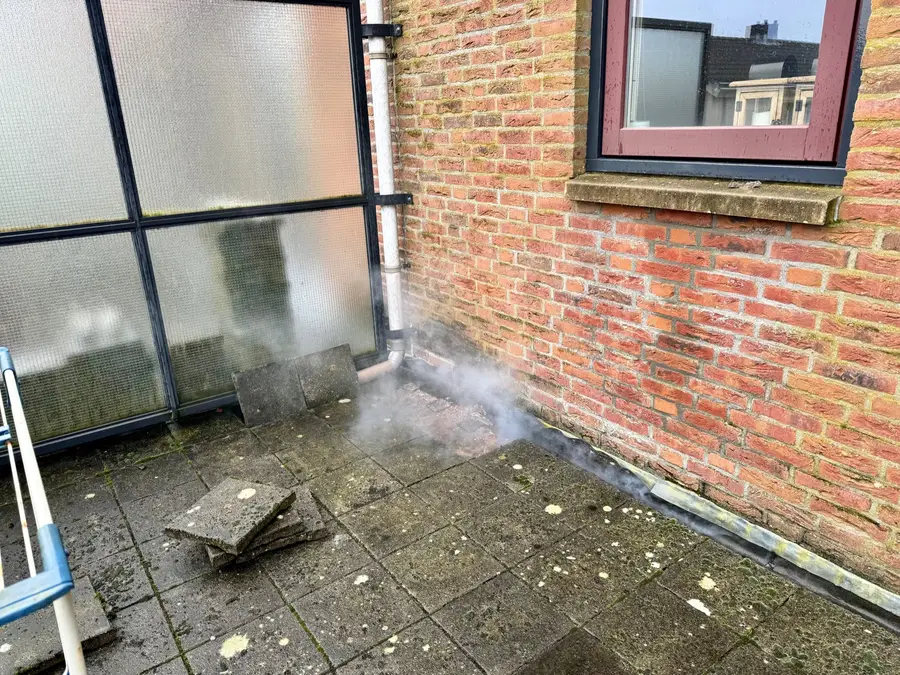 Rook ontsnapt bij de aansluiting van een plat dak op de gevel